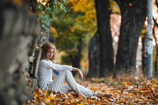 La ragazza si siede tra le foglie d'autunno