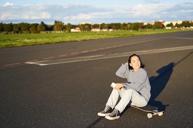 La ragazza skater si siede sul suo skateboard su strada utilizzando lo smartphone in chat sull'app mobile