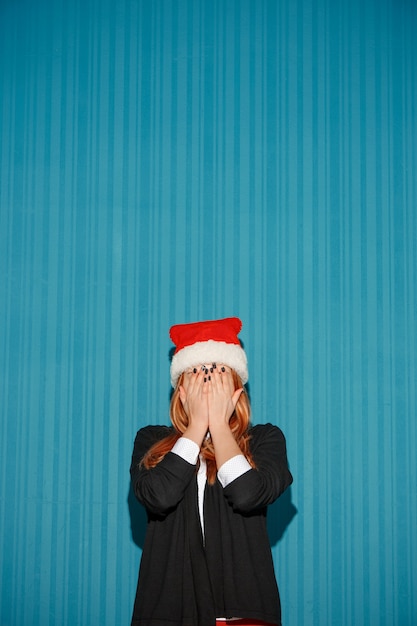 La ragazza sorpresa di natale che porta un cappello della Santa sui precedenti blu