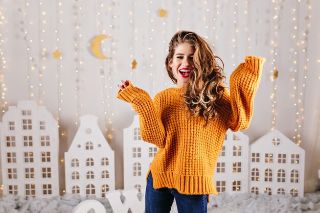 La ragazza sorpresa e allegra ride felice nell'atmosfera accogliente del nuovo anno, posando per il ritratto in maglione lavorato a maglia Over Size
