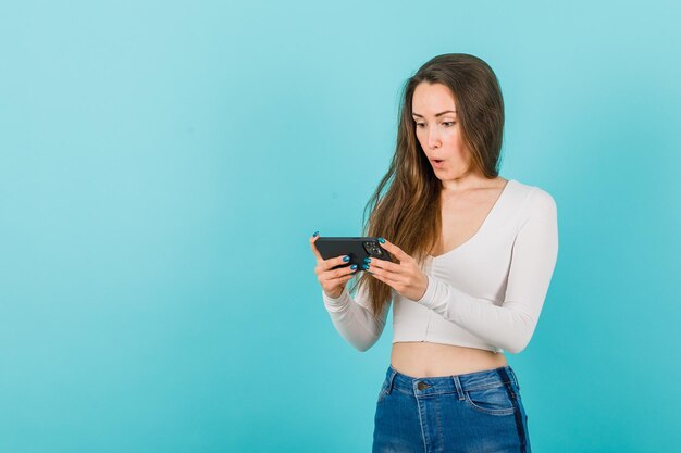 La ragazza sorpresa sta guardando lo schermo dello smartphone su sfondo blu