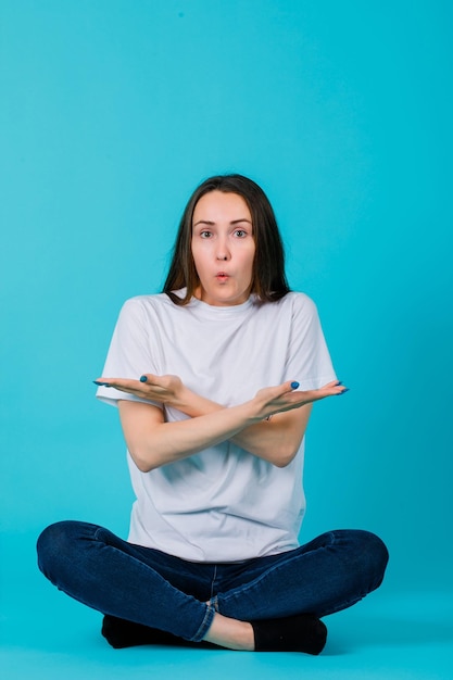 La ragazza sorpresa sta indicando in giro con le mani incrociate su sfondo blu