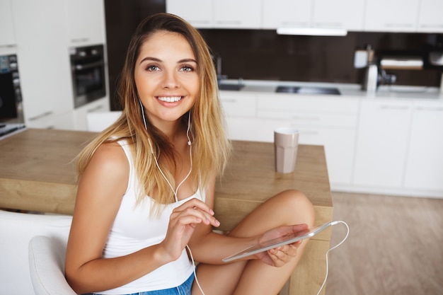 La ragazza sorridente attraente che si siede alla cucina e ascolta la musica.
