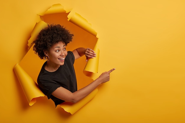 La ragazza sorridente dall'aspetto gioioso e amichevole punta da parte con un'espressione felice, un sorriso a trentadue denti, felice di mostrare una pubblicità fantastica