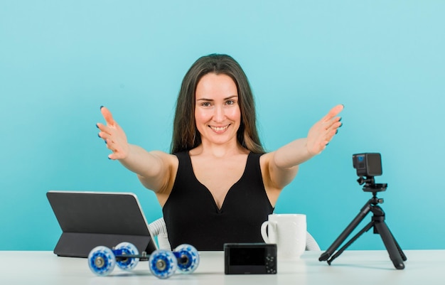 La ragazza sorridente del blogger sta estendendo le mani alla fotocamera su sfondo blu