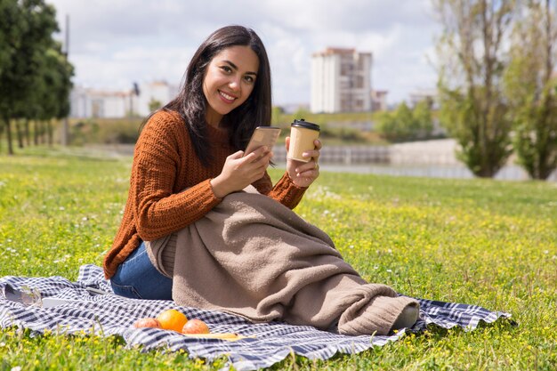 La ragazza sorridente dello studente si è avvolta in caffè bevente del plaid