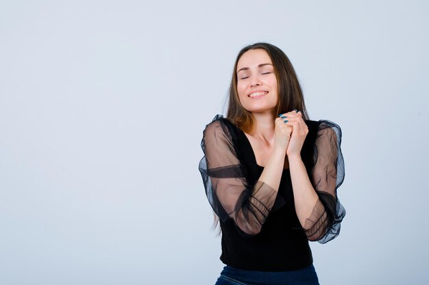 La ragazza sorridente desidera tenendo le mani insieme su sfondo bianco