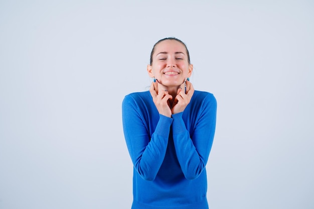 La ragazza sorridente desidera tenendo le mani sotto il mento su sfondo bianco