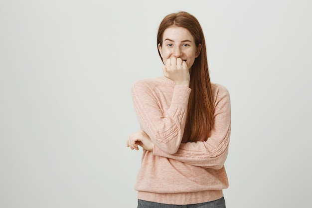 La ragazza sorridente divertente della testarossa ridacchia e copre la bocca, ascolta la barzelletta