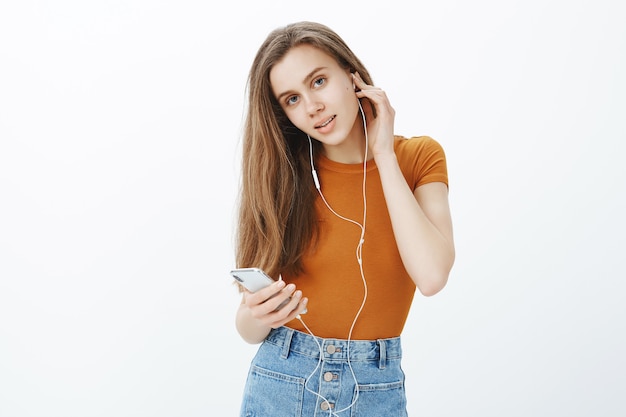 La ragazza sorridente felice ha messo le cuffie, ascolta il podcast o la musica sul telefono cellulare