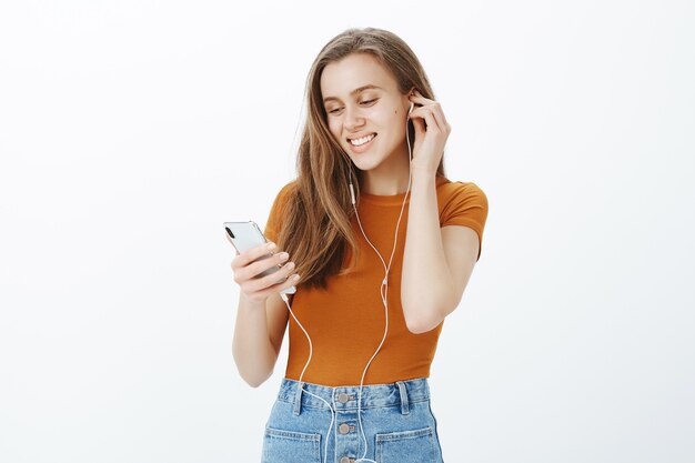 La ragazza sorridente felice ha messo le cuffie, ascolta il podcast o la musica sul telefono cellulare