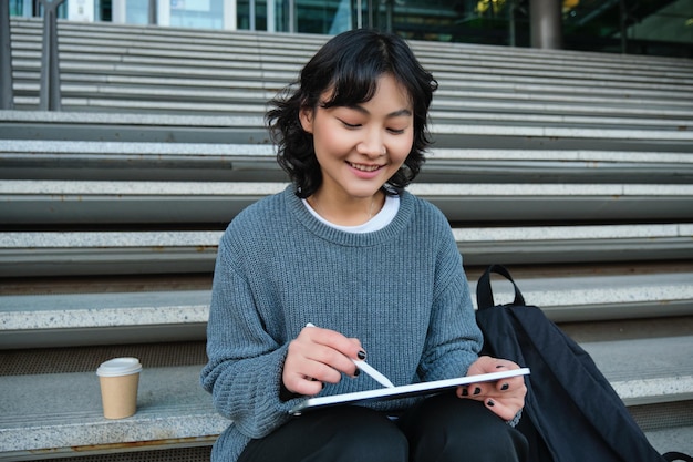 La ragazza sorridente graphic designer che utilizza la tavoletta digitale e lo strumento penna per disegnare fa l'assegnazione a casa per l'uni