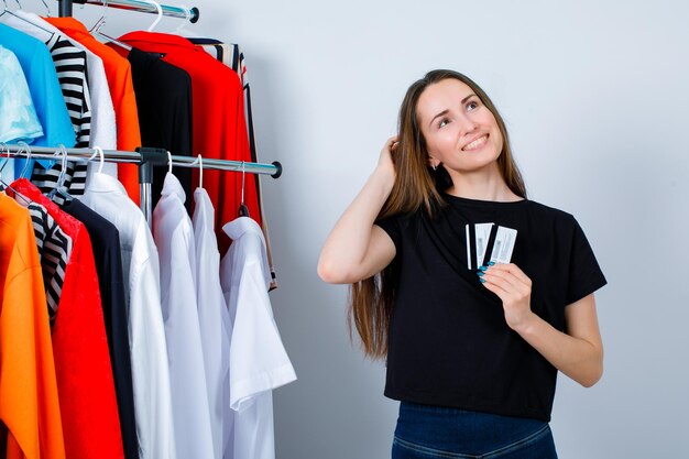 La ragazza sorridente sta alzando lo sguardo tenendo le carte di credito sullo sfondo dei vestiti