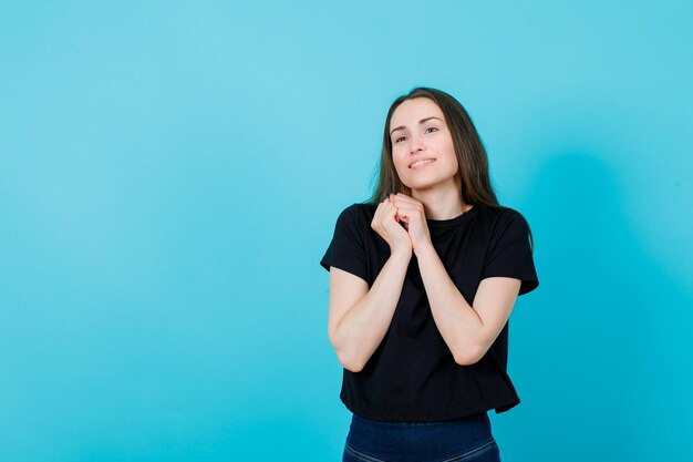 La ragazza sorridente sta distogliendo lo sguardo tenendo le mani insieme sul petto su sfondo blu