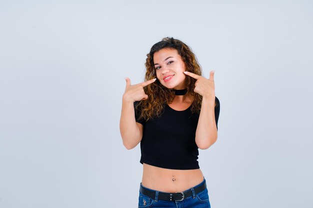 La ragazza sorridente sta indicando il suo sorriso con gli indici su priorità bassa bianca