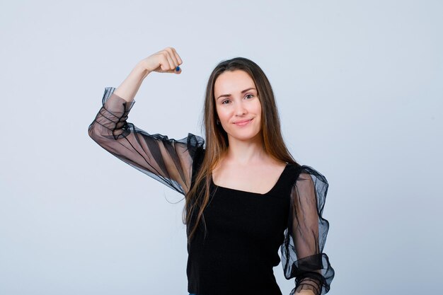 La ragazza sorridente sta mostrando i suoi muscoli alzando il pugno su sfondo bianco