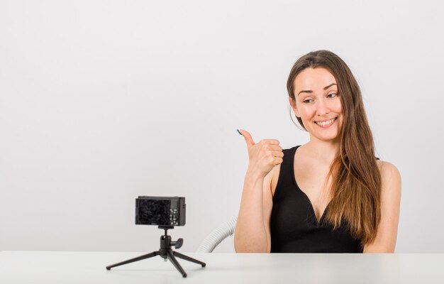 La ragazza sorridente sta posando alla macchina fotografica mostrando il suo pollice su fondo bianco