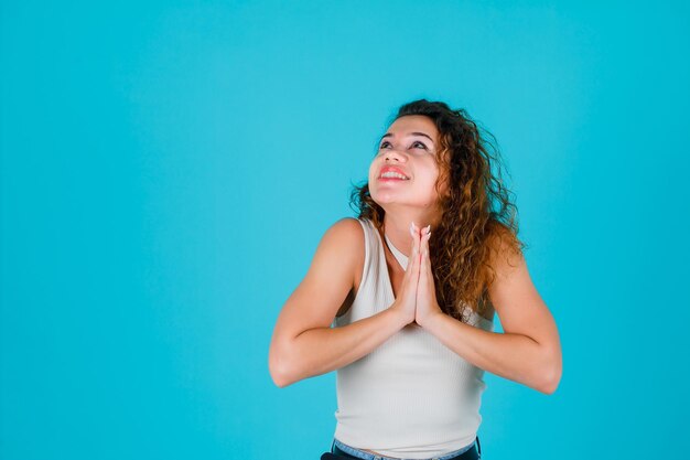 La ragazza sorridente sta pregando tenendo le mani insieme sul petto su sfondo blu