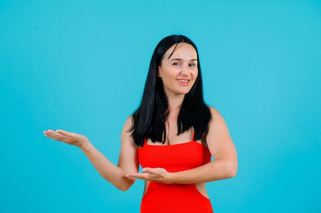 La ragazza sorridente sta puntando a sinistra con le mani su sfondo blu