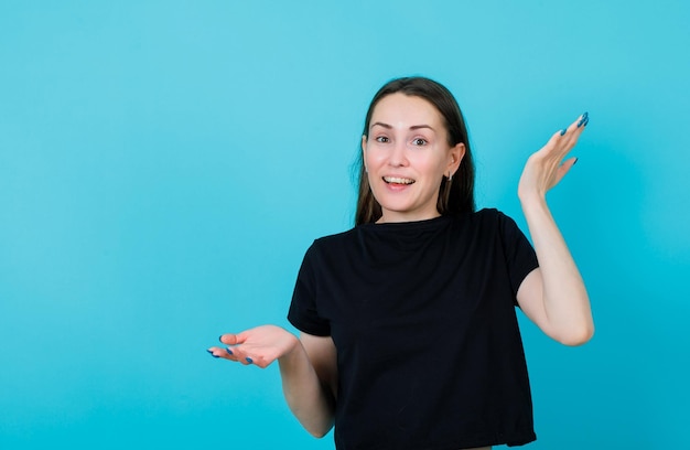 La ragazza sorridente sta puntando su e giù aprendo le mani larghe su sfondo blu