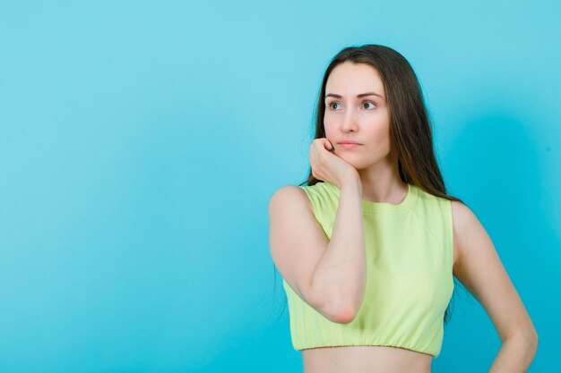 La ragazza sta distogliendo lo sguardo mettendo la mano sotto il mento su sfondo blu