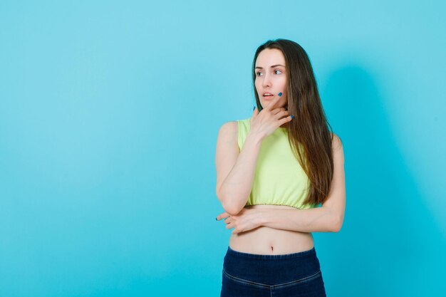 La ragazza sta guardando almeno mettendo la mano sul mento su sfondo blu