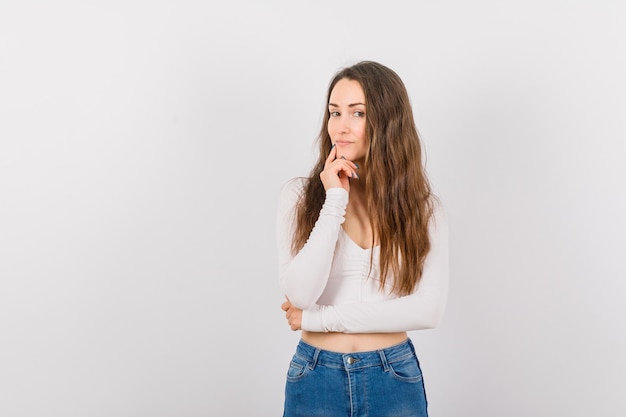 La ragazza sta guardando la fotocamera tenendo l'indice sul mento su sfondo bianco