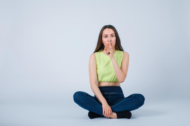 La ragazza sta mostrando il gesto di silenzio sedendosi sul pavimento su fondo bianco