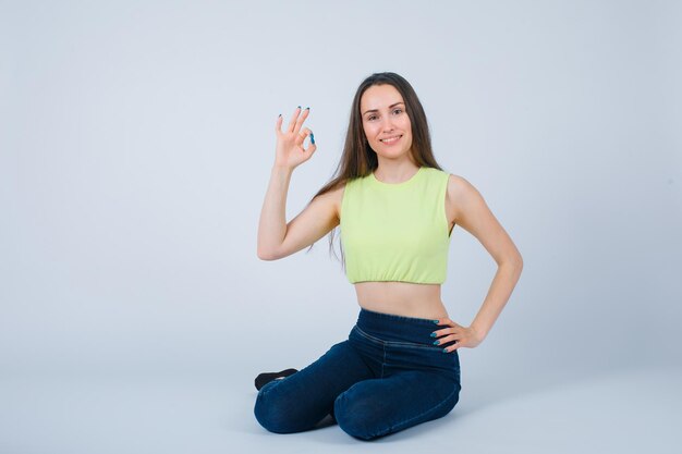 La ragazza sta mostrando il gesto giusto sedendosi sul pavimento su fondo bianco