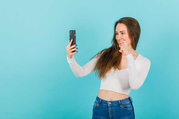 La ragazza sta prendendo selfie mostrando il gesto delle dimensioni con l'altra mano su sfondo blu