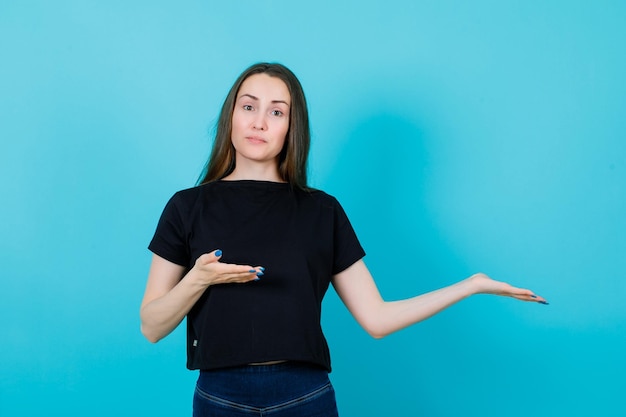 La ragazza sta puntando a destra con le mani su sfondo blu