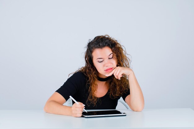 La ragazza sta scrivendo mettendo la mano sul mento su fondo bianco