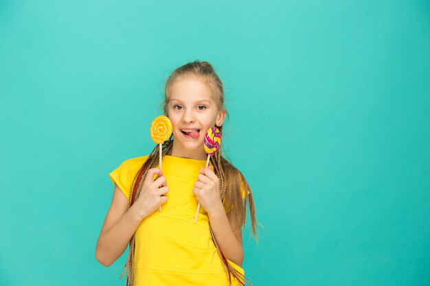 La ragazza teenager con la lecca-lecca variopinta su una parete blu