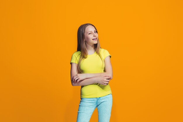 La ragazza teenager felice che sta e che sorride contro la parete arancio