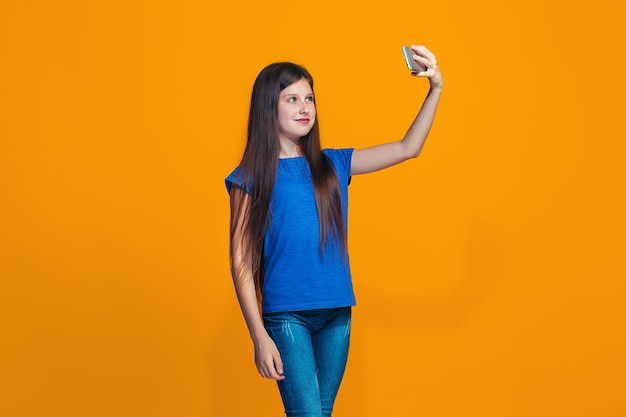 La ragazza teenager felice in piedi e sorridente contro l'arancio.