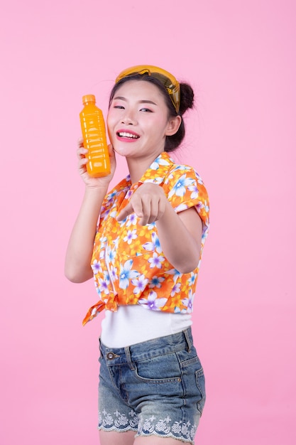 La ragazza tiene una bottiglia di succo d&#39;arancia su uno sfondo rosa.