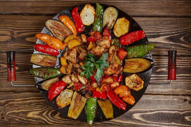 La salvia di pollo con patate peperone e melanzane cotta sulla vista superiore del carbone