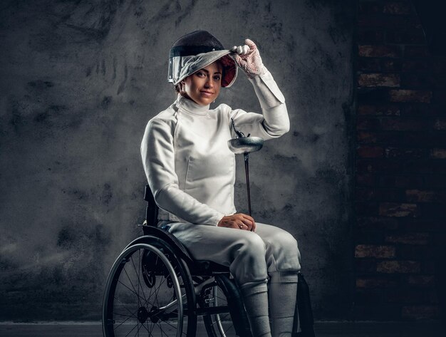 La schermitrice femminile in sedia a rotelle tiene una maschera di sicurezza e una spada.