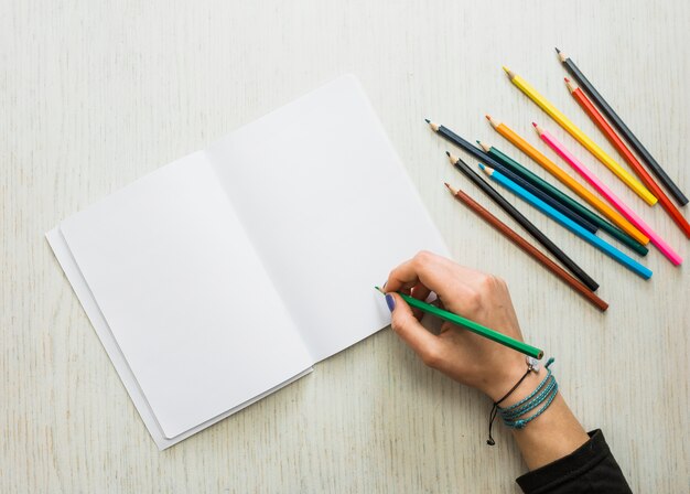 La scrittura della mano della persona sul libro bianco in bianco facendo uso della matita di colore