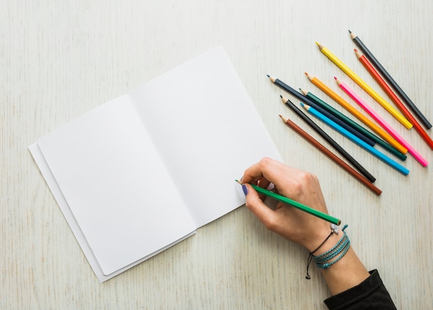 La scrittura della mano della persona sul libro bianco in bianco facendo uso della matita di colore