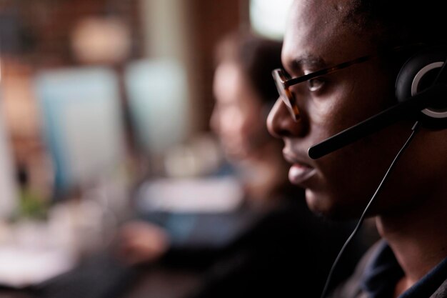 La segretaria dell'helpdesk ascolta il cliente durante una chiamata di assistenza, utilizzando la rete del servizio clienti sull'auricolare. Receptionist maschio che lavora all'assistenza di telemarketing del call center. Avvicinamento.