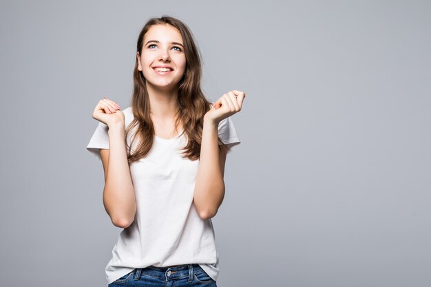 La signora abbastanza felice in maglietta bianca e jeans blu rimane davanti al fondo bianco dello studio