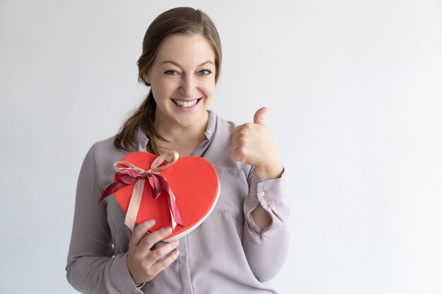 La signora allegra che mostra il cuore ha modellato il contenitore ed il pollice di regalo su