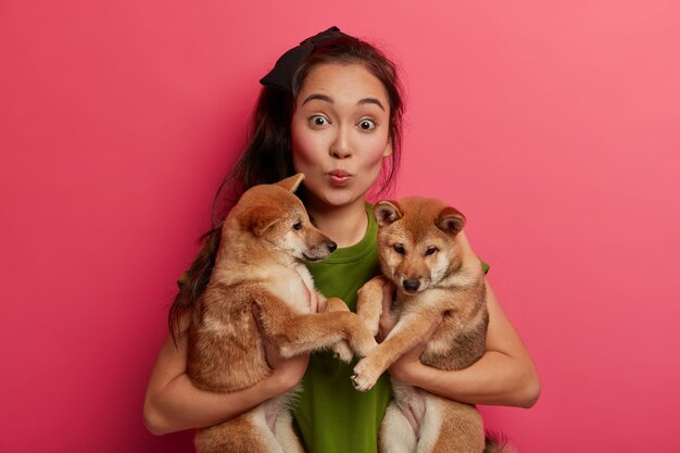 La signora asiatica sorpresa tiene le labbra piegate, posa con due cuccioli, porta alla clinica veterinaria.