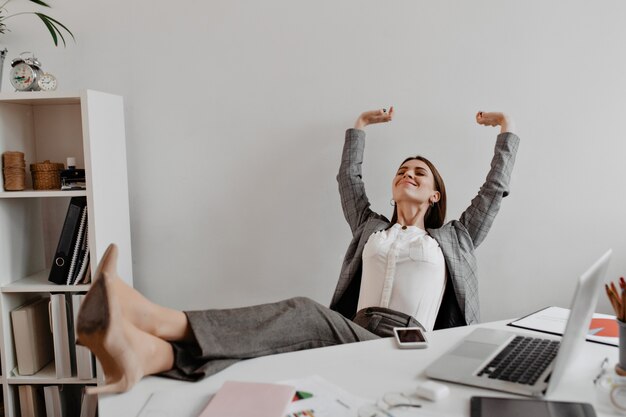 La signora di affari soddisfatta del risultato di lavoro con piacere ha gettato le gambe sul desktop bianco.