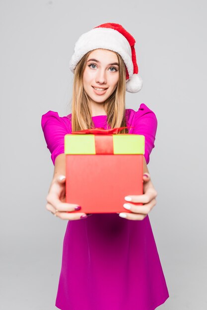 La signora divertente abbastanza sorridente in breve vestito rosa e cappello del nuovo anno tiene la sorpresa della scatola di carta nelle sue mani