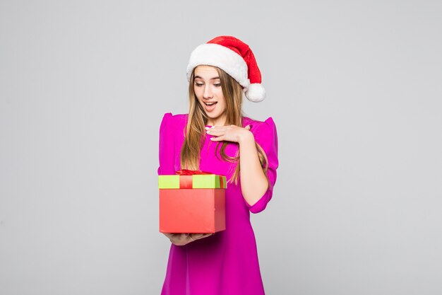 La signora divertente abbastanza sorridente in breve vestito rosa e cappello del nuovo anno tiene la sorpresa della scatola di carta nelle sue mani