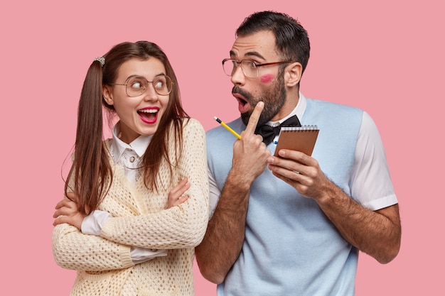 La signora positiva in vecchia camicetta alla moda tiene le braccia conserte, il ragazzo sorpreso indica la traccia del bacio con il rossetto rosso, flirta con il compagno di classe