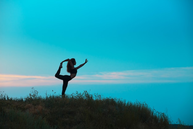 La silhouette della giovane donna sta praticando lo yoga