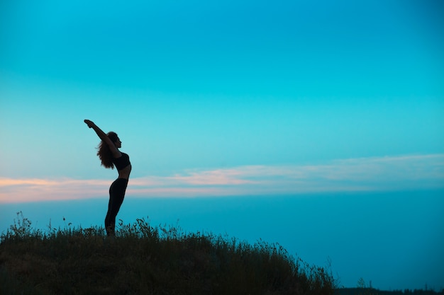 La silhouette della giovane donna sta praticando yoga